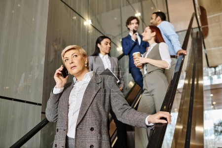 Una mujer de negocios en acción, hablando en un teléfono celular mientras está de pie en una escalera mecánica en movimiento.