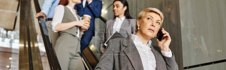 Photo for A woman multitasks, talking on a cell phone while walking down an escalator. - Royalty Free Image
