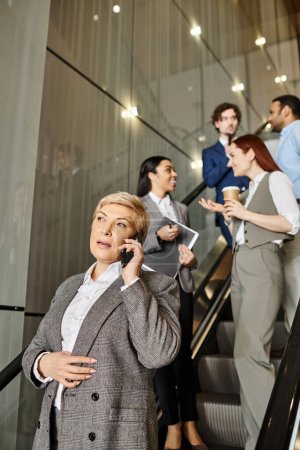 Eine Frau multifunktional auf einer Rolltreppe, telefoniert mit einem Handy.