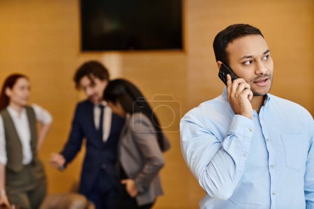 Photo for A man stands in front of an interracial group, speaking on a cell phone. - Royalty Free Image