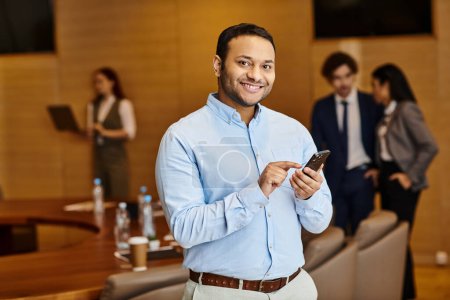 A man of diverse ethnicity stands in a conference room, engaging on a cell phone.