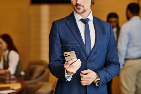 Téléchargez les photos : A diverse businessman in a suit confidently holds a cell phone. - en image libre de droit