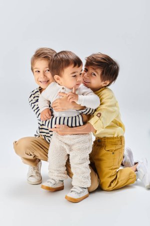 A group of young children, sit together in a studio against a grey backdrop.