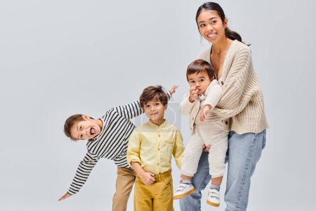 Asian mother gracefully poses with her children in a studio against a grey backdrop, glowing with love and joy.