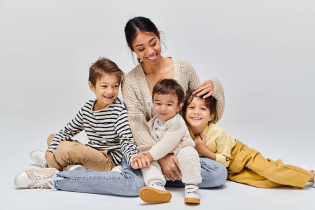 Photo for A young Asian mother sitting on the ground with her children, interacting and creating a special bond in a studio setting. - Royalty Free Image