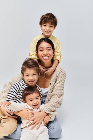 Téléchargez les photos : Une jeune mère asiatique pose avec amour avec ses enfants dans un studio, sur un fond gris doux. - en image libre de droit