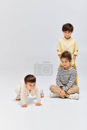 Three young boys are peacefully seated on the ground in front of a white background, exuding a sense of calm.