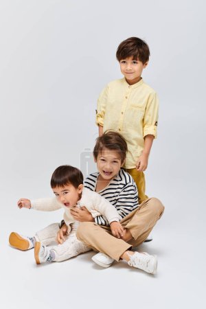 A trio of children, seated on the floor, engage in playful interaction with one another in a cozy studio setting.
