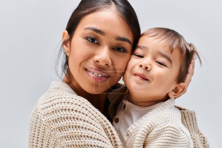 Téléchargez les photos : Une jeune mère asiatique tient tendrement son enfant dans ses bras dans un studio sur fond gris. - en image libre de droit