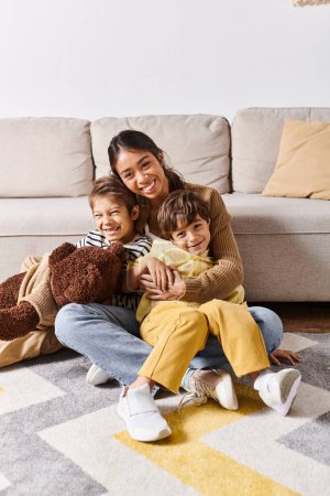Foto de Una joven madre asiática sentada en el suelo con sus dos hijos pequeños en la acogedora sala de estar en casa. - Imagen libre de derechos