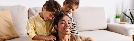 Téléchargez les photos : A young Asian mother sits on a couch surrounded by her two little sons in their cozy living room, sharing a moment of peace. - en image libre de droit