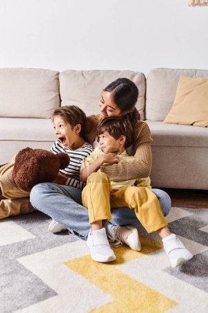 Eine junge asiatische Mutter sitzt mit ihren beiden kleinen Söhnen im gemütlichen Wohnzimmer auf dem Boden.