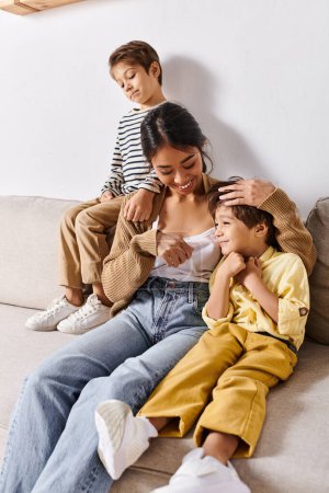 Photo for A young Asian mother sits on a couch with her two little sons, sharing a moment of quiet togetherness in the cozy living room. - Royalty Free Image