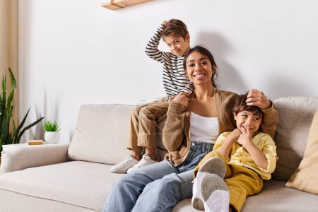 Téléchargez les photos : Une jeune mère asiatique et ses deux petits fils assis sur un canapé confortable dans leur salon, partageant un moment de convivialité. - en image libre de droit