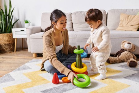 A young Asian mother lovingly interacts with her little son while playing on the floor in their cozy living room.
