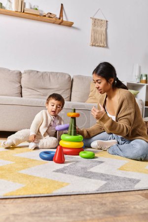 Foto de Una joven madre asiática felizmente se involucra con su pequeño hijo en el piso de la sala de estar, jugando y riendo juntos. - Imagen libre de derechos