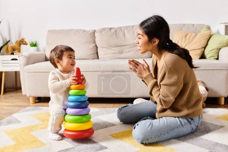 Foto de Una joven madre asiática jugando felizmente con su pequeño hijo en el suelo en su acogedora sala de estar. - Imagen libre de derechos