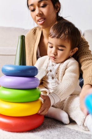 Foto de A young Asian mother and her little son happily playing with a stack of toys in the living room. - Imagen libre de derechos