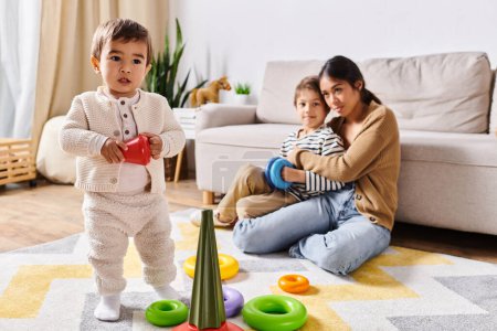 Eine junge asiatische Mutter und ihre beiden kleinen Söhne spielen fröhlich mit Spielzeug in ihrem gemütlichen Wohnzimmer.