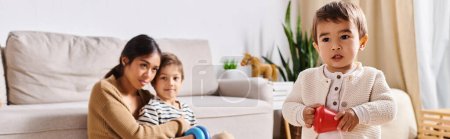 Téléchargez les photos : A young Asian mother and her two little sons sit closely together on a cozy couch in their living room. - en image libre de droit