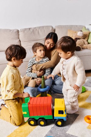 a young Asian mother and her little sons, energetically playing together with a toy truck in their living room.