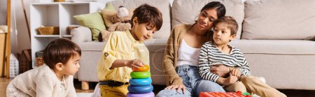 Eine junge asiatische Mutter und ihre kleinen Söhne spielen fröhlich mit einem Stapelspielzeug im Wohnzimmer.