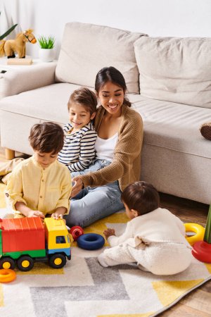 Foto de Una joven madre asiática felizmente se sienta en el suelo, jugando con sus hijos pequeños en la acogedora sala de estar en casa. - Imagen libre de derechos