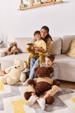 A young Asian mother sits on a couch with her little sons, surrounded by teddy bears, engaged in a cozy cuddle session.