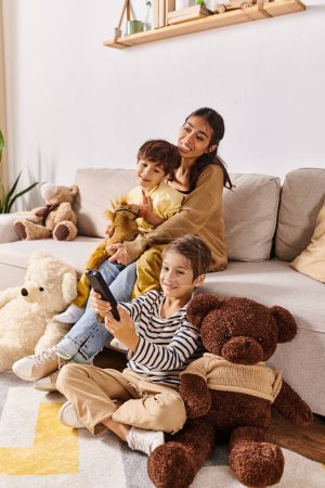 Junge asiatische Mutter und ihre kleinen Söhne sitzen auf einer Couch, umgeben von Teddybären im heimischen Wohnzimmer.