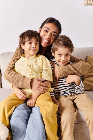 A young Asian mother sits on a couch, surrounded by her two energetic little sons, in their cozy living room at home.