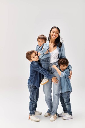 A young Asian mother posing with her little sons, all dressed in denim, capturing a heartwarming moment in a grey studio.