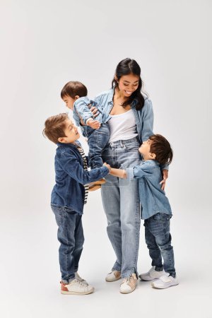 Junge asiatische Mutter und ihre drei Söhne, alle in Jeans gekleidet, stehen vereint vor einem schlichten weißen Hintergrund.