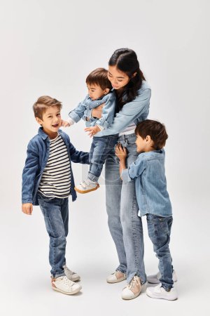 Foto de Un grupo de niños, incluyendo una joven madre asiática y sus hijos pequeños, de pie uno al lado del otro en un estudio gris, todos con ropa de mezclilla. - Imagen libre de derechos