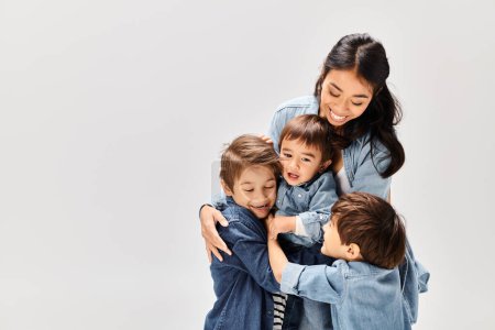 Foto de Una joven madre asiática abraza a sus dos hijos pequeños, todos vestidos con denim, creando un momento conmovedor de amor y conexión. - Imagen libre de derechos