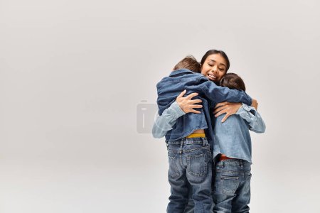 Photo for A young Asian mother and her little sons, wearing denim clothes, hugging each other in front of a white background. - Royalty Free Image