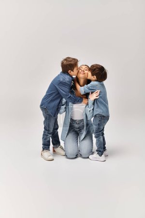 Téléchargez les photos : Une mère avec ses fils, s'embrassant dans un studio gris tout en portant des vêtements en denim. - en image libre de droit