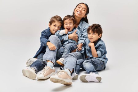 Eine junge asiatische Mutter sitzt mit ihren drei kleinen Söhnen auf dem Boden, alle in Jeanskleidung, und schafft eine herzerwärmende Szene.