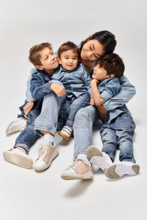 Photo for A group of young children wearing denim clothes sit closely together in a grey studio, accompanied by their Asian mother. - Royalty Free Image