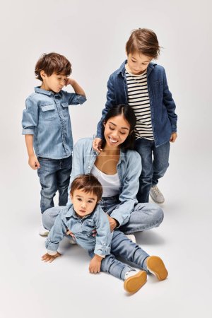 Une jeune mère asiatique et ses petits fils, tous vêtus de denim, posant pour une photo dans un studio gris.