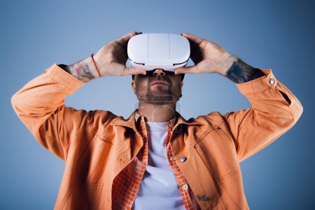 Photo for A man in an orange shirt raises a white vr headset above his head in a studio setting. - Royalty Free Image