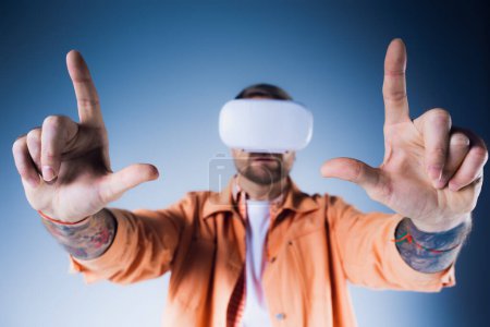 Téléchargez les photos : Un homme dans un casque VR, les yeux bandés avec un bandeau, fait signer le Vulcain avec confiance dans un cadre studio. - en image libre de droit