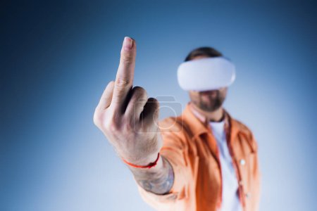 A man, blindfolded and wearing a VR headset, points confidently towards an unseen target in a studio setting, middle finger