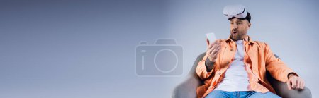 Photo for A man in an orange shirt confidently holds a cell phone in his hand. - Royalty Free Image