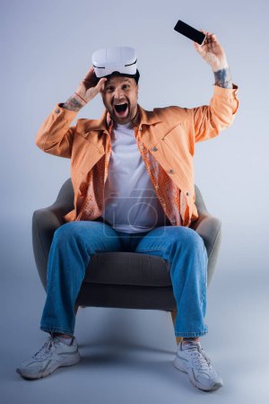 Téléchargez les photos : Un homme assis confortablement sur une chaise portant un casque vr, perdu dans la pensée. - en image libre de droit