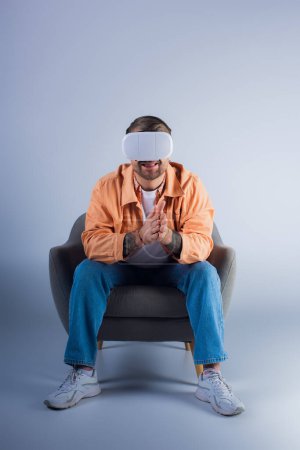 Photo for A man in a chair wearing a blindfold, lost in virtual world with a VR headset, in a studio. - Royalty Free Image