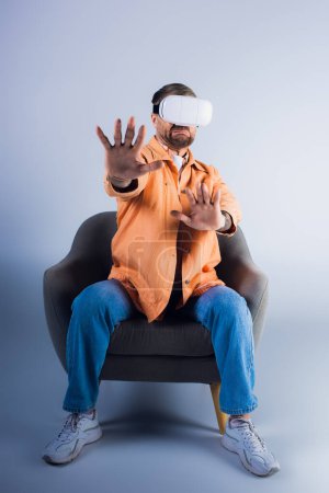 A man in virtual reality headset sits in a chair with his hands up, immersed in a virtual world in a studio setting.