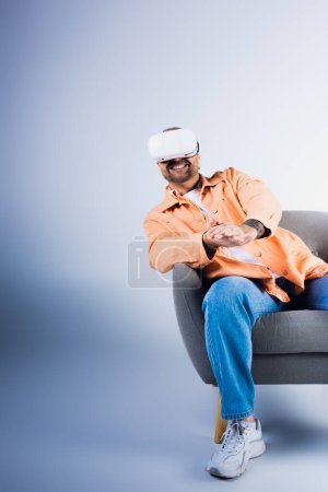Téléchargez les photos : Un homme heureux portant un casque VR est assis sur une chaise dans un cadre de studio. - en image libre de droit