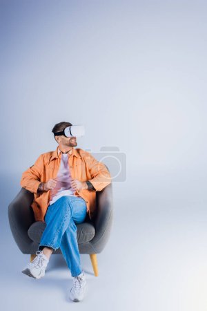 A man in a VR headset comfortably lounging in a chair in a studio setting.