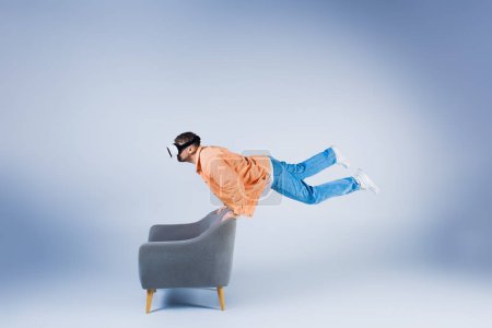 Un homme en chemise orange et casque vr montre son agilité, équilibrant et exécutant un tour sur une chaise dans un cadre de studio.