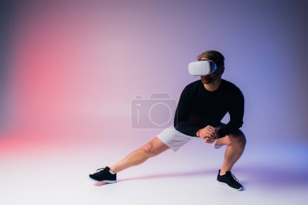 Un hombre con una camisa negra y pantalones cortos blancos se adentra en la realidad virtual mientras usa un auricular en un entorno de estudio.
